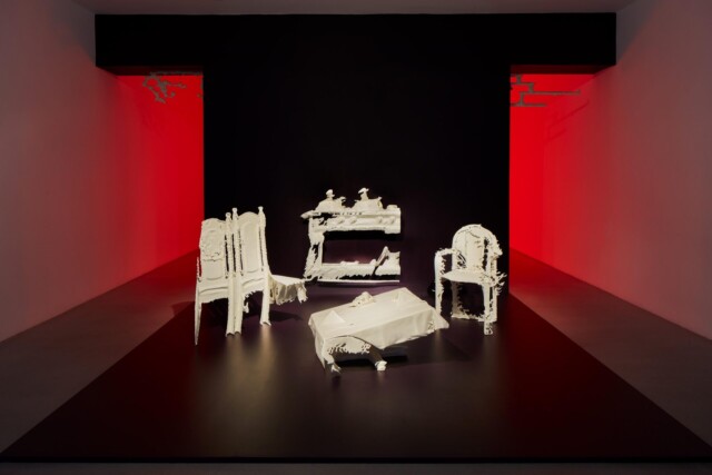 Kuvassa installaatio, jossa punaisten seinien keskellä on rikkinäisiä koristeellisia valkoisia huonekaluja