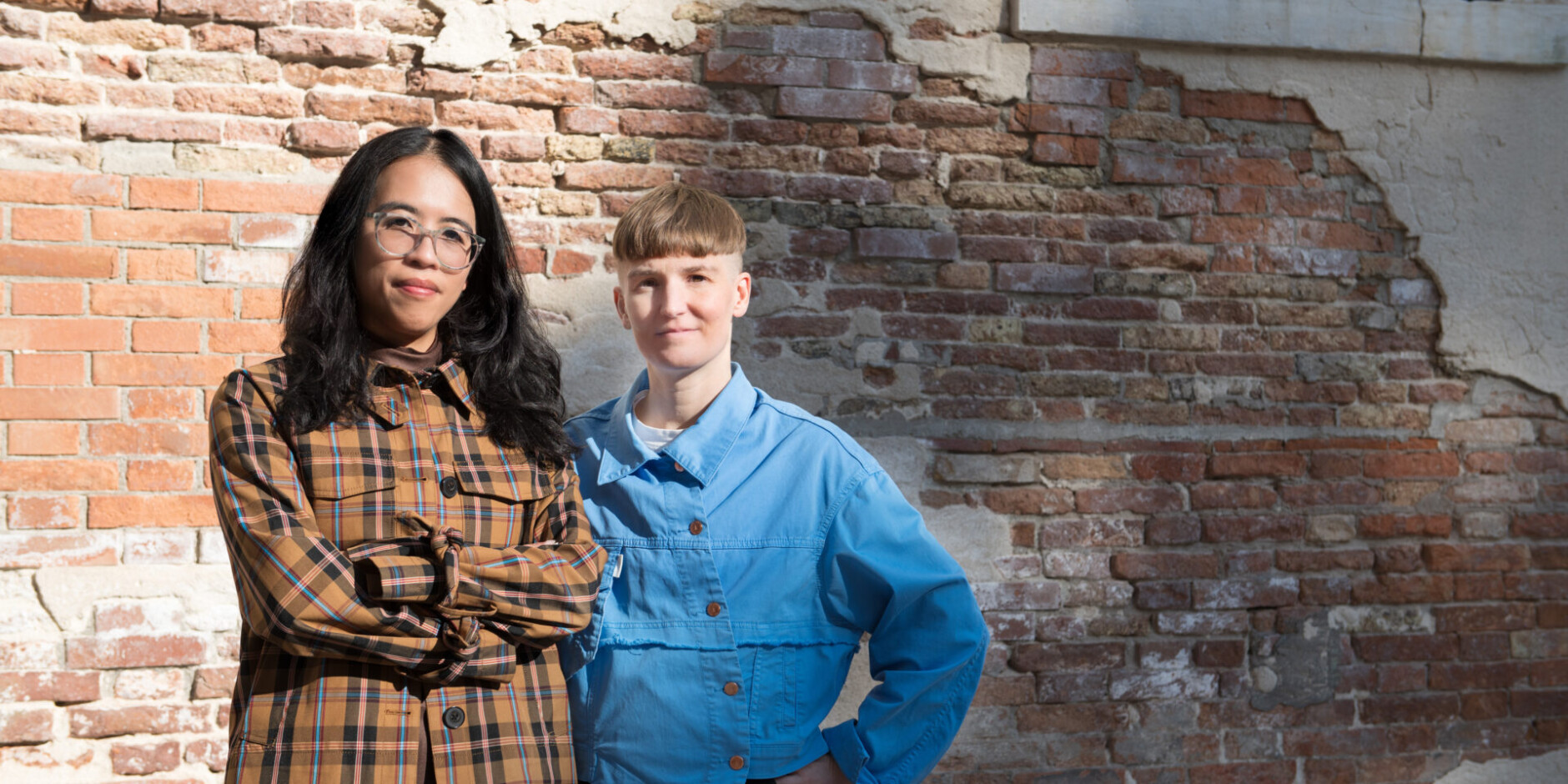 Kuraattori Christina Li ja taiteilija Pilvi Takala seisovat punatiiliseinän edessä.